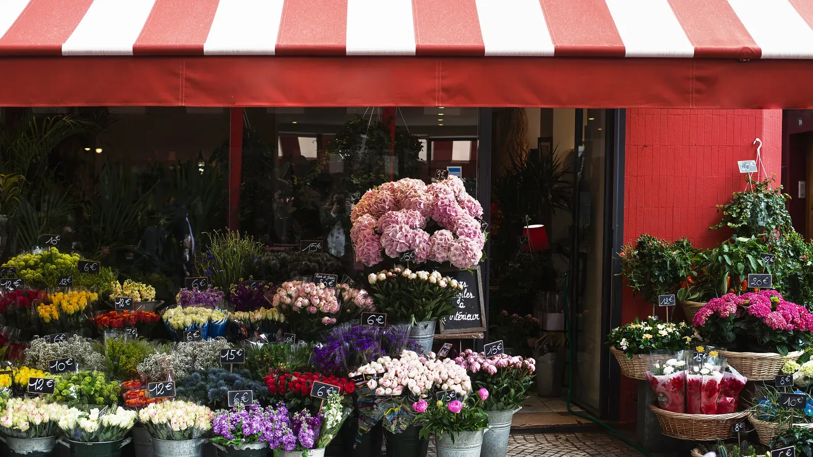 A flower shop with buckets full of bouquets under an awning.