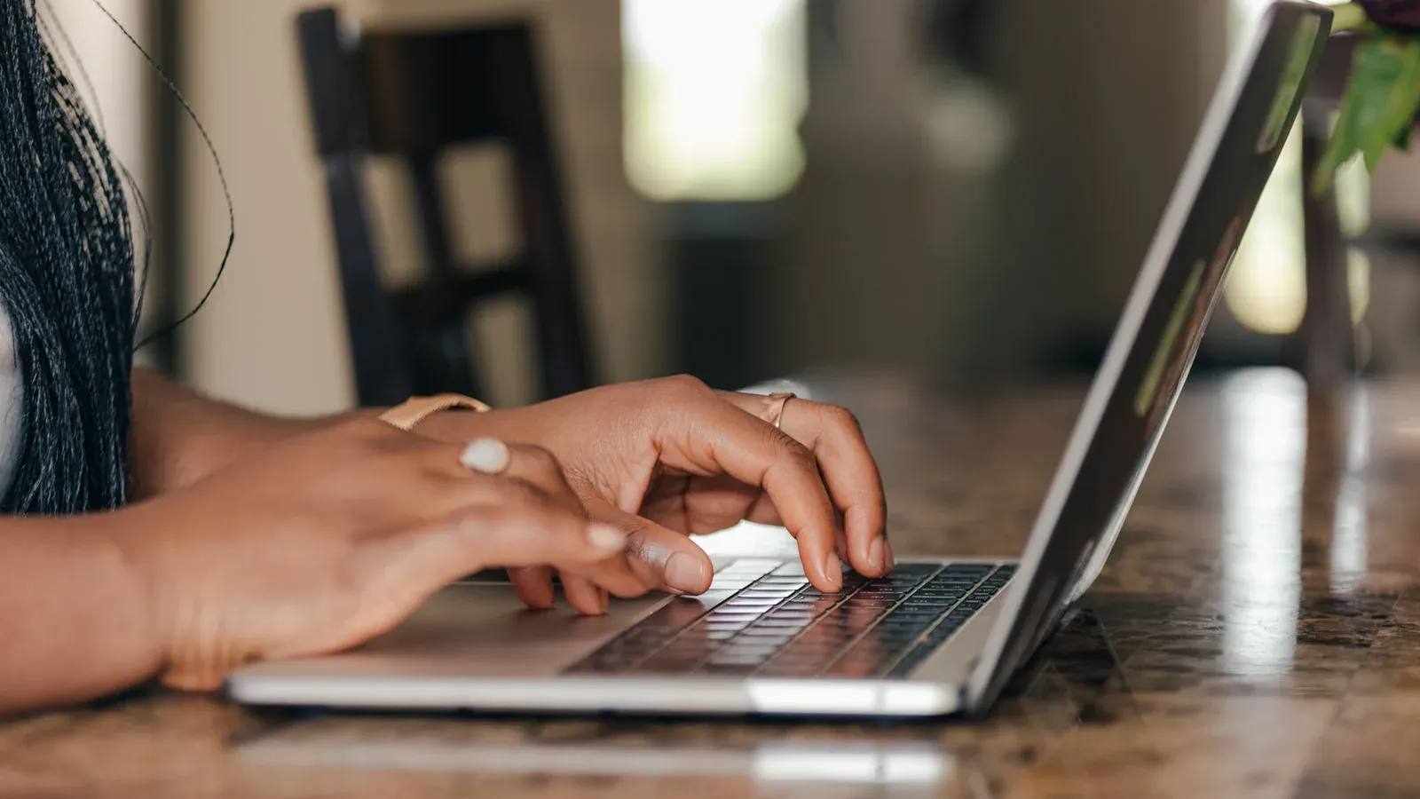 Hands typing on a laptop at a wooden table.