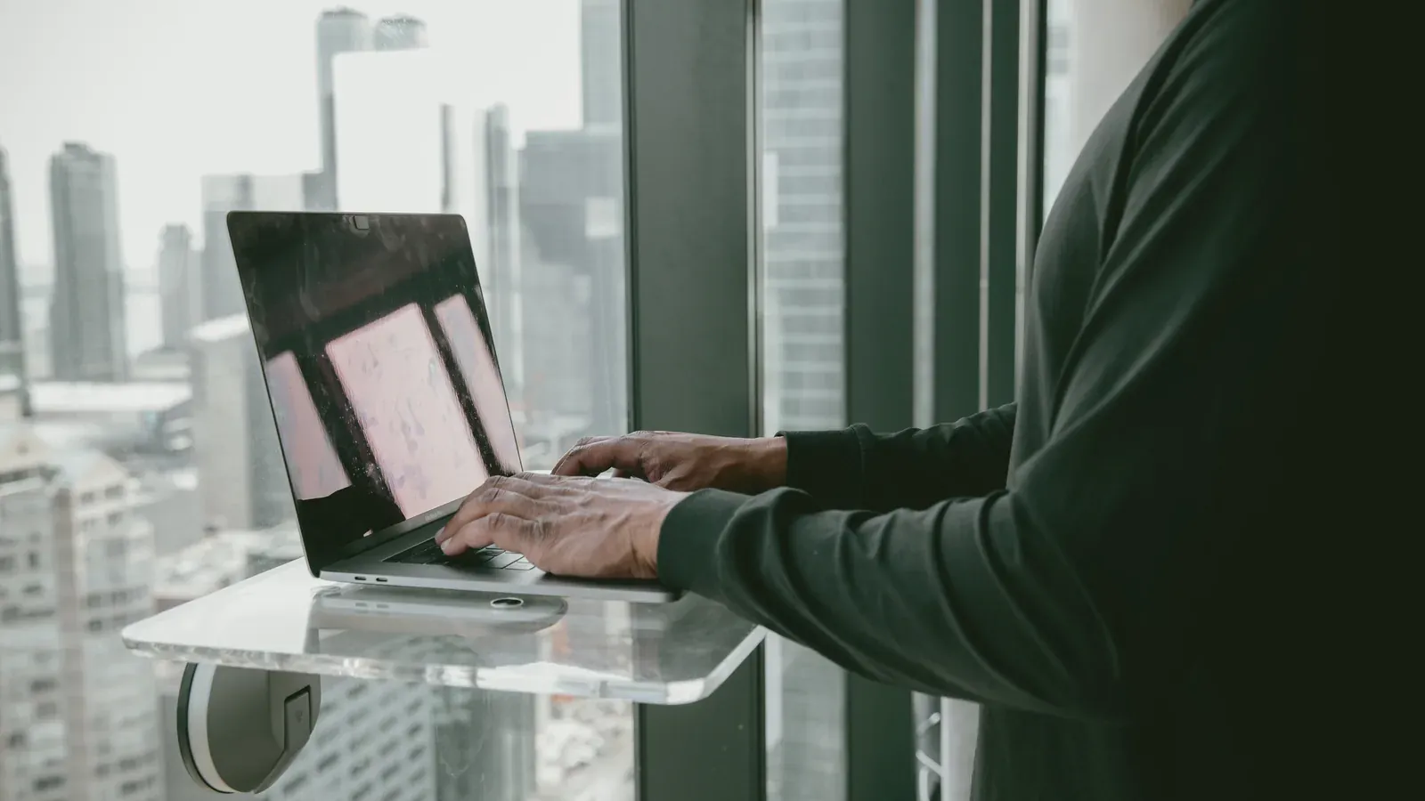 Someone works on a laptop by a window overlooking the city.